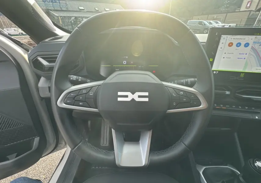 Vue intérieure centrée sur le volant cuir du Dacia Duster TCE 130 4x2 Journey 2025 avec écran tactile et levier de vitesse manuel.