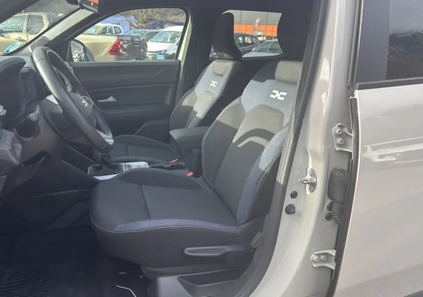 Vue intérieure côté conducteur du Dacia Duster 2025 Sandstone, sièges tissu avec logo distinctif et volant cuir soft feel.