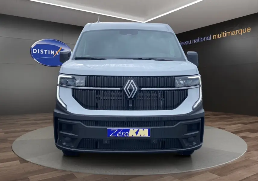 Vue frontale d’un Renault Master blanc avec calandre noire et phares LED, sur fond intérieur showroom multimarque.