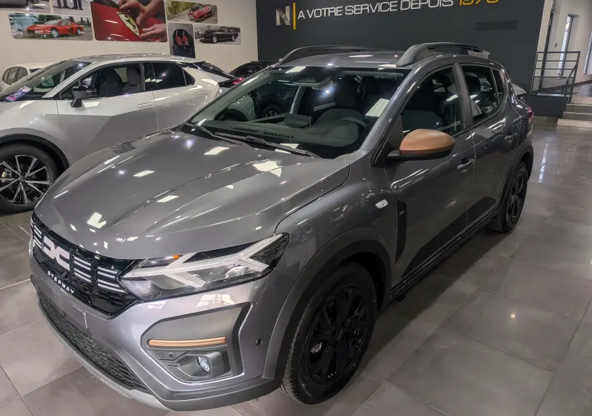 Vue 3/4 avant droite d'une Dacia Sandero Stepway TCe 110 Gris Schiste avec rétroviseurs couleur cuivre en showroom.