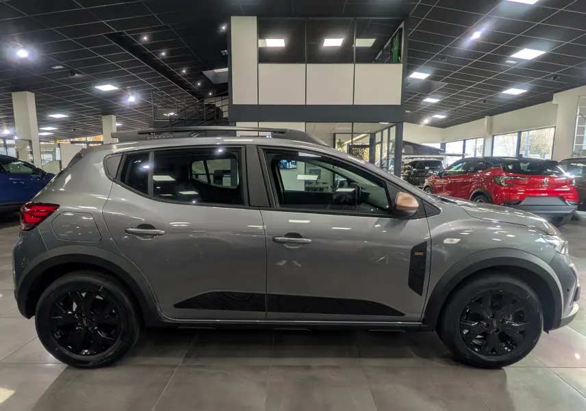 Profil droit d'une Dacia Sandero Stepway TCe 110 Gris Schiste avec jantes noires et détails noirs sur les portes, en showroom.
