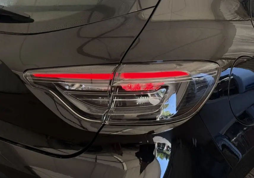 Feu arrière droit allumé sur Renault Clio noir, vue rapprochée du côté arrière du véhicule.