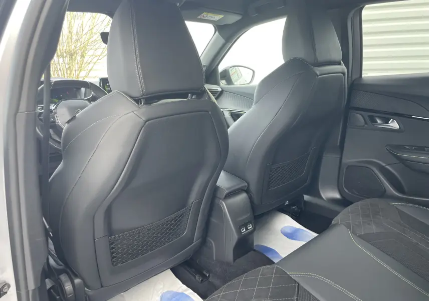 Vue intérieure arrière du Peugeot 2008 gris Artense 2022, sièges avant en cuir noir avec surpiqûres vertes et ports USB centraux.