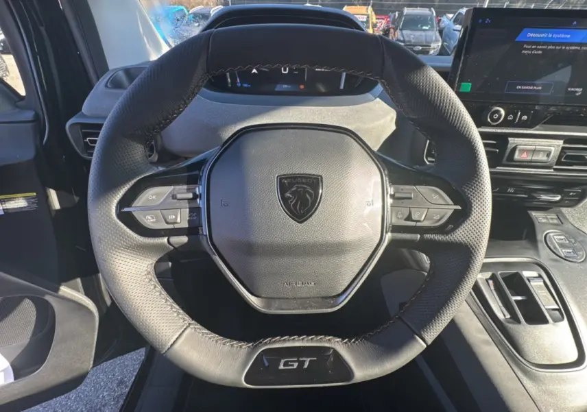 Vue rapprochée du volant cuir multifonctions noir avec logo Peugeot et badge GT du Rifter 2025, intérieur moderne.