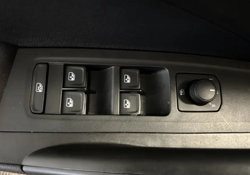 Gros plan sur les commandes de lève-vitres et réglage des rétroviseurs côté conducteur de la Skoda Fabia 2023 gris argent.