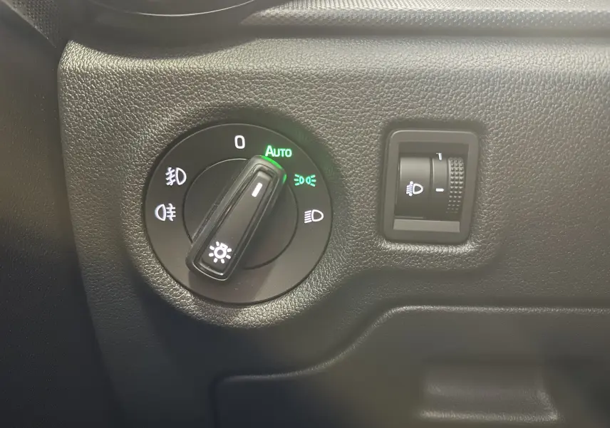 Gros plan sur le sélecteur de phares avec réglage automatique dans l’habitacle noir d’une Skoda Fabia 2023 gris argent.