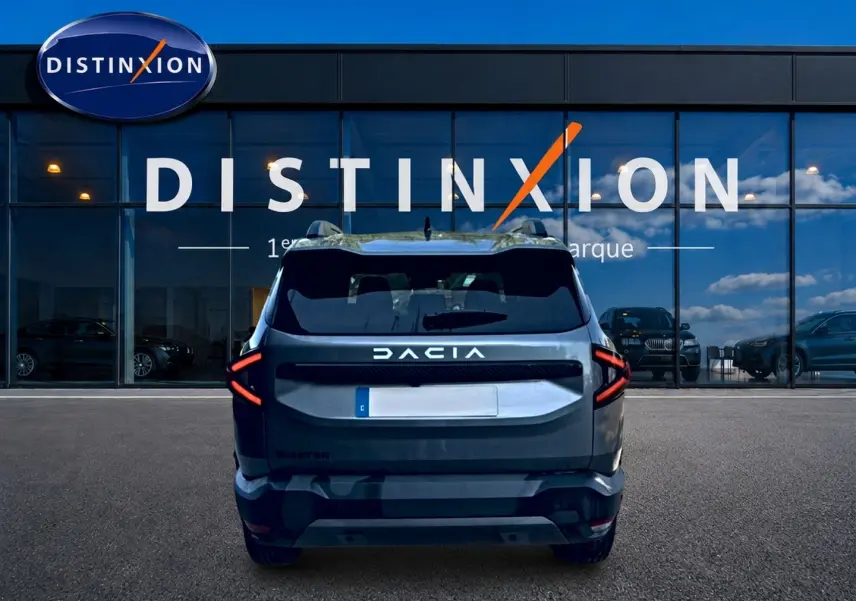 Vue arrière d'un Dacia Bigster gris schiste garé devant une vitrine avec logo Distinxion, feux arrière LED en forme de flèche.