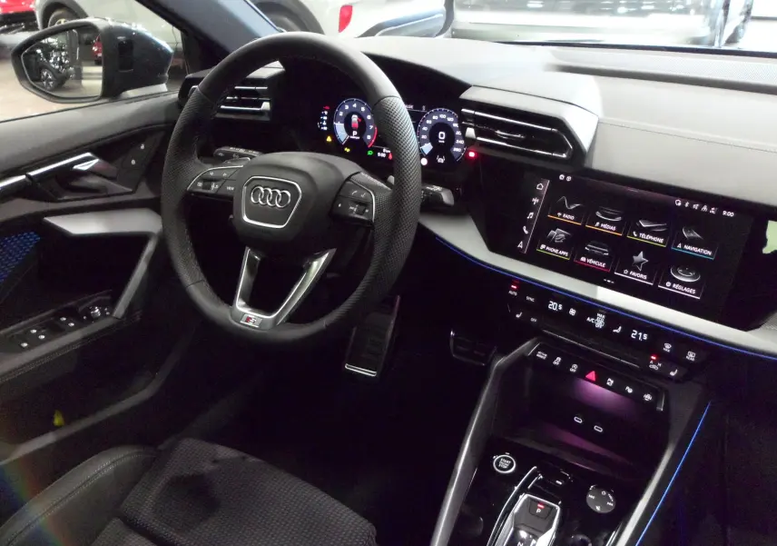 Vue intérieure côté conducteur de l'Audi A3 Sportback 35 TFSI 150 S-Line 2025 avec tableau de bord numérique et ambiance lumineuse bleue
