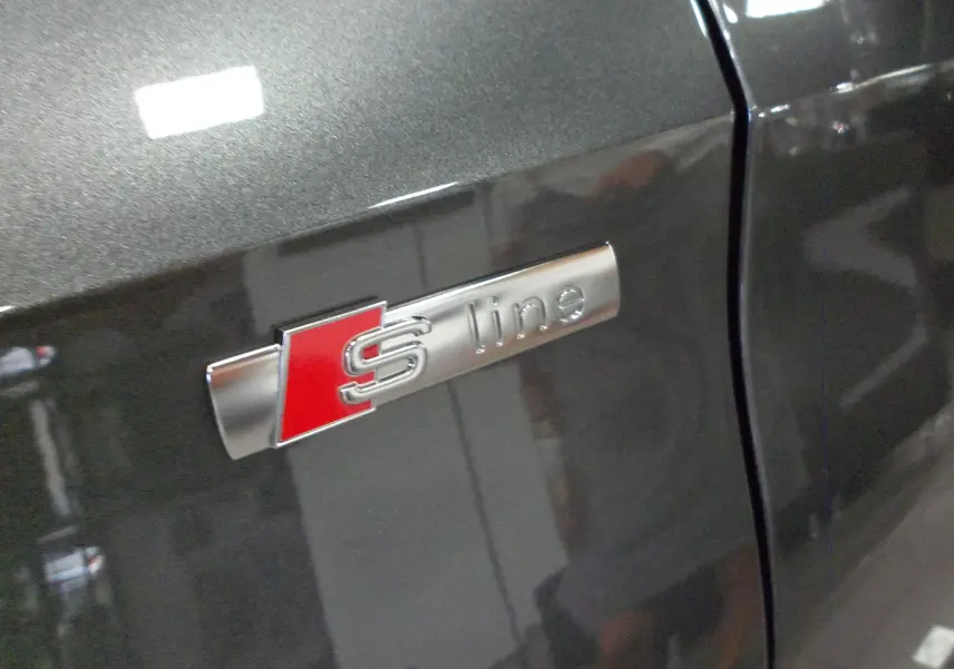 Gros plan sur l'emblème S line argent et rouge sur la porte gris Daytona d'une Audi A3 Sportback 2025.