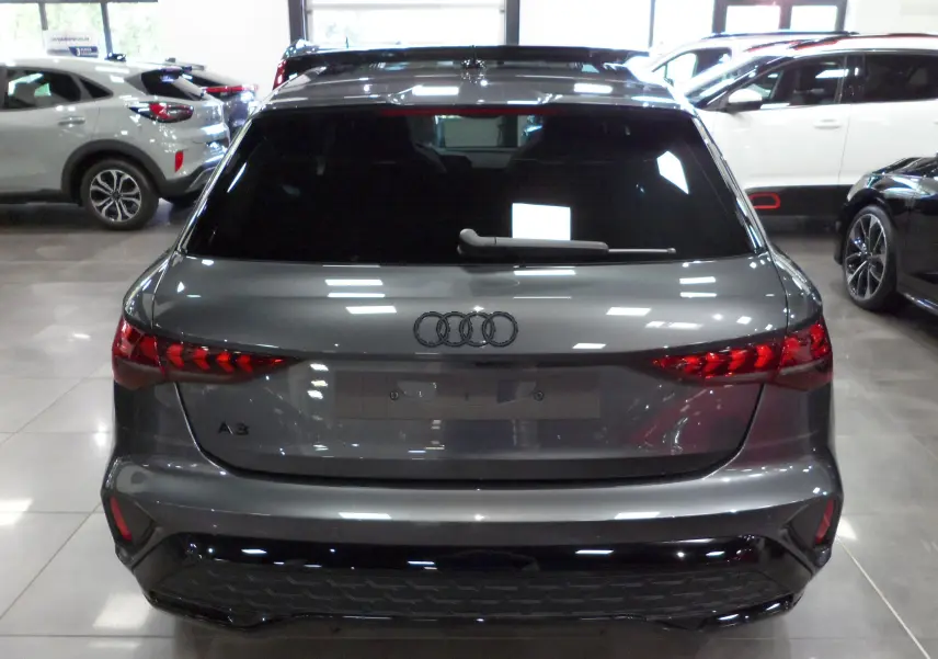 Vue arrière d'une Audi A3 Sportback 35 TFSI gris Daytona avec feux LED et pare-chocs noir brillant en showroom.