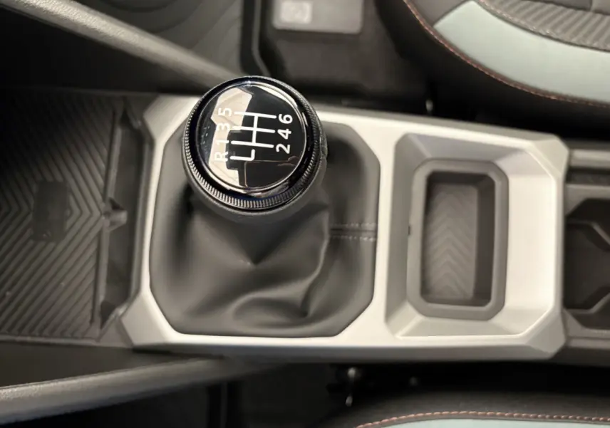 Le levier de vitesses manuel noir du Dacia Duster 2025, vue plongeante sur la console centrale et les sièges partiellement visibles.