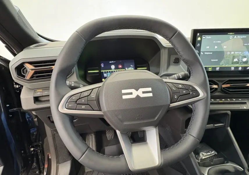 Vue intérieure centrée sur le volant cuir noir du Dacia Duster 2025 avec tableau de bord digital et écran tactile.