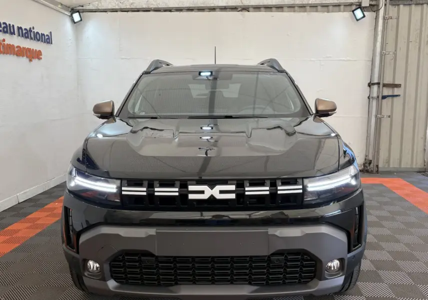 Vue frontale d'un Dacia Duster noir 2025 avec phares LED allumés et calandre distinctive au logo central.