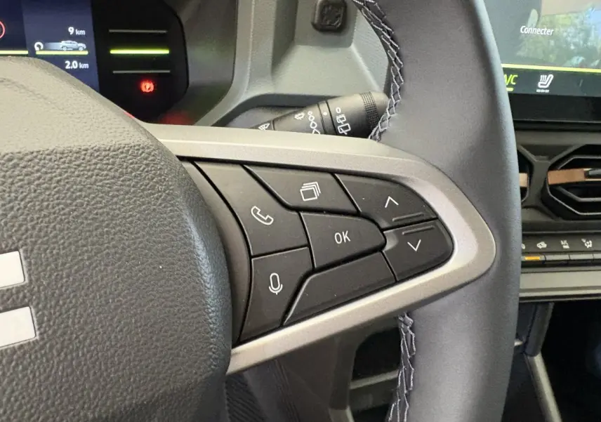 Gros plan sur le côté droit du volant noir du Dacia Duster 2025 avec commandes multifonctions et écran tactile en arrière-plan