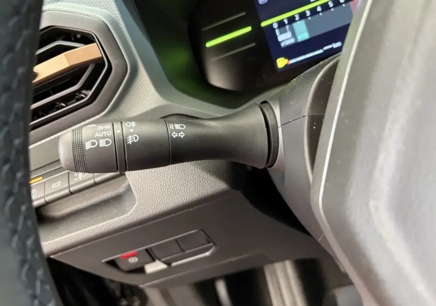Gros plan sur la manette de clignotants et commandes lumineuses du tableau de bord du Dacia Duster noir 2025.