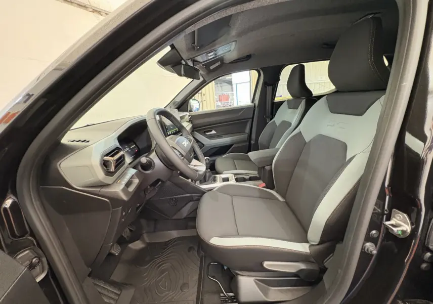 Intérieur avant droit du Dacia Duster noir 2025, sièges bicolores gris et noir avec volant multifonctions en vue latérale.