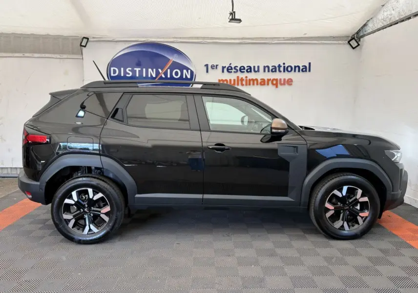 Profil côté gauche du Dacia Duster noir 2025 avec jantes alliage bicolores et barres de toit noires.