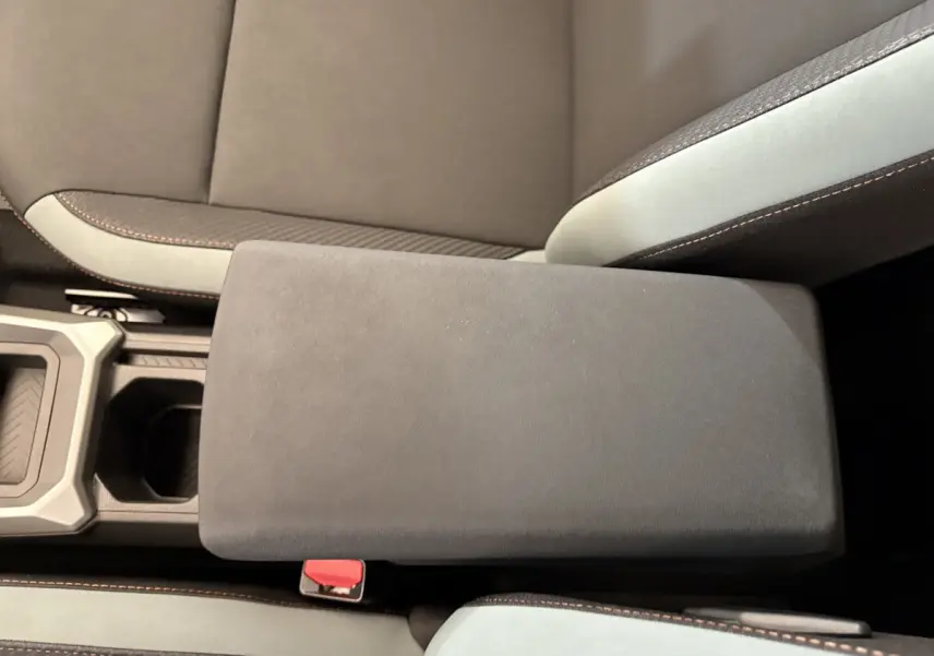 Gros plan sur l'accoudoir central noir et les sièges bicolores gris et noir du Dacia Duster 2025 hybride.