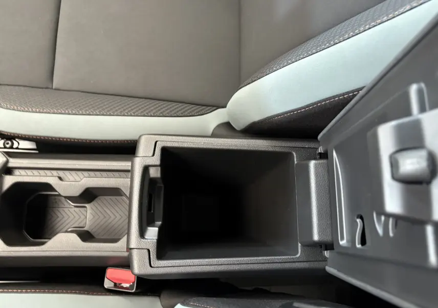 Gros plan sur la console centrale ouverte du Dacia Duster noir 2025, montrant le rangement intérieur et les sièges tissu gris.