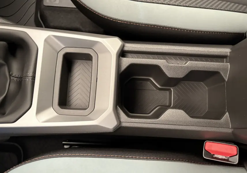 Gros plan sur la console centrale du Dacia Duster 2025 noir, avec porte-gobelets et surpiqûres orange sur les sièges.