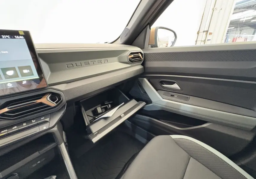 Intérieur côté passager du Dacia Duster noir 2025, tableau de bord avec boîte à gants ouverte et écran tactile visible.
