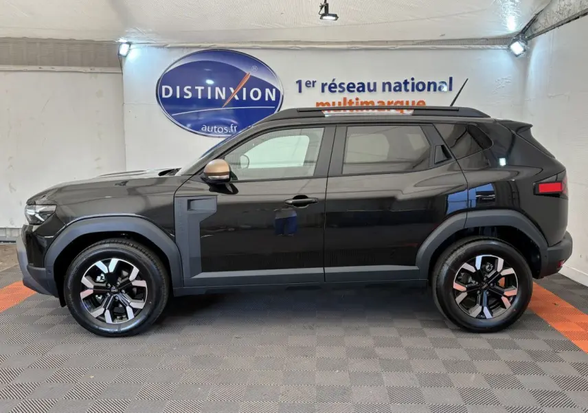 Profil côté gauche du Dacia Duster noir 2025 avec jantes bicolores et barres de toit noires en intérieur showroom.