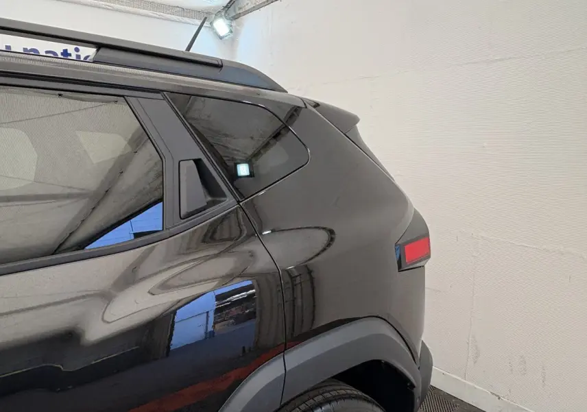 Vue arrière côté gauche du Dacia Duster noir 2025 avec feux arrière rectangulaires et barres de toit noires.