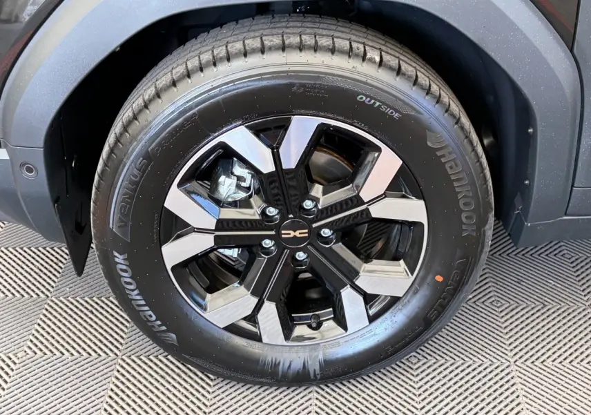 Gros plan sur la roue avant droite noire du Dacia Duster 2025 avec jante alliage bicolore et logo central.