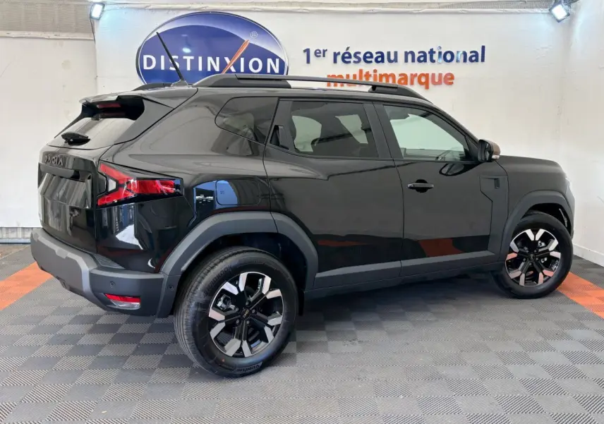 Vue latérale droite du Dacia Duster noir 2025 avec jantes alliage et barres de toit noires dans un showroom.