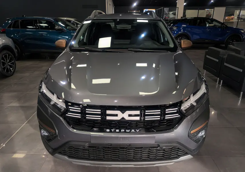 Vue frontale d'une DACIA Sandero Stepway TCe 110 gris schiste avec calandre noire et détails cuivrés en showroom.