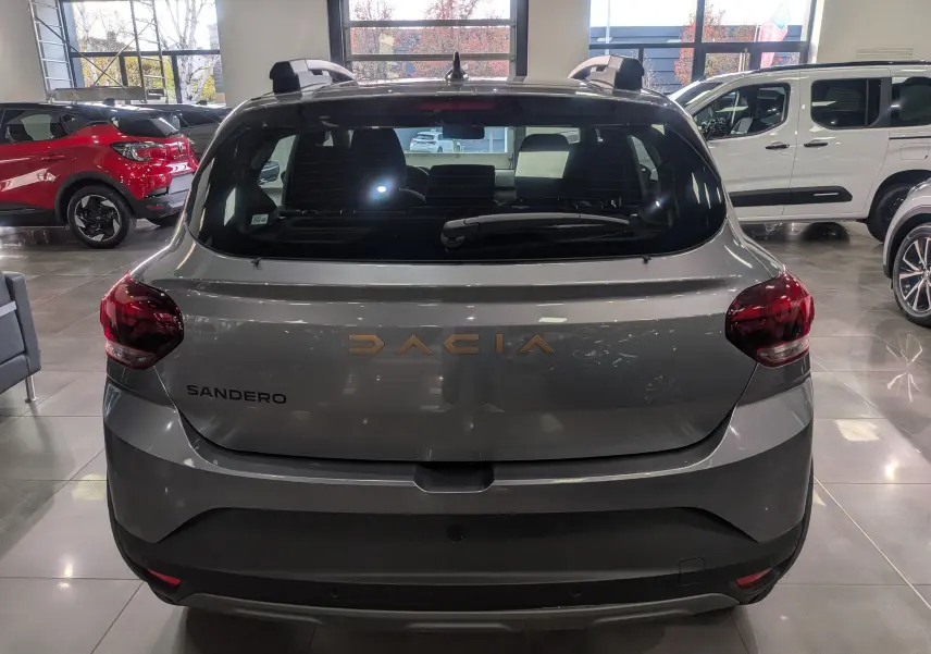 Vue arrière d'une Dacia Sandero Stepway gris schiste, avec logo DACIA en lettres dorées dans un showroom.