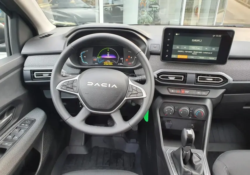 Vue intérieure frontale du tableau de bord du Dacia Jogger 2024, avec volant multifonction, écran tactile et levier de boîte auto.