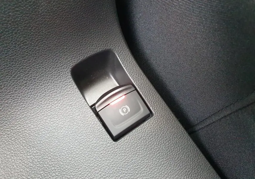 Gros plan sur le bouton de frein de parking électrique avec témoin rouge, intérieur noir du Dacia Jogger 2024.