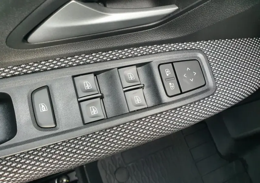 Gros plan sur la commande des vitres et rétroviseurs côté conducteur avec habillage tissu gris et noir.
