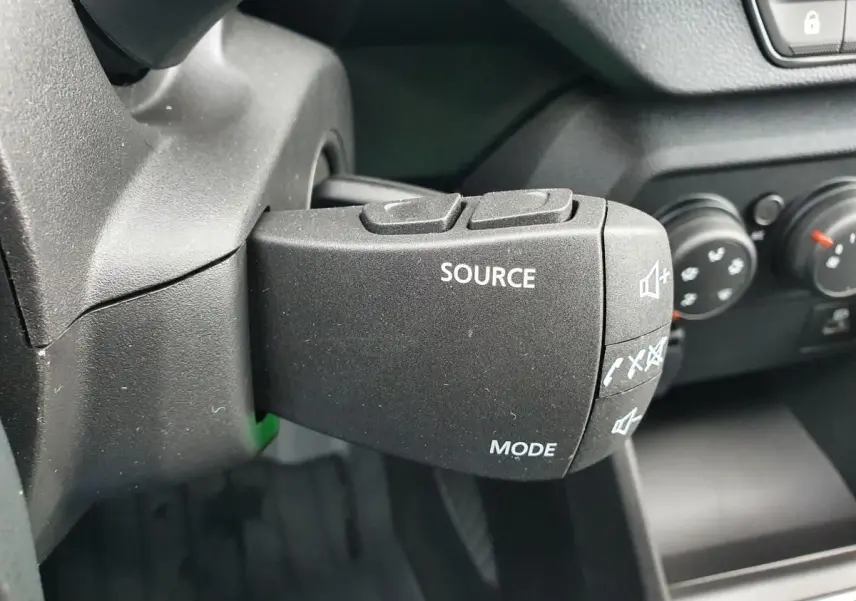 Gros plan sur la commande audio au volant du Dacia Jogger 2024, intérieur noir avec boutons source et mode visibles.