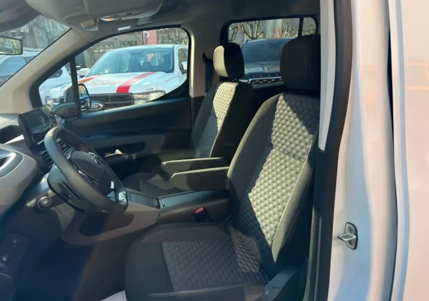 Vue intérieure côté gauche du Peugeot Rifter blanc kaolin 2025, mettant en valeur les sièges tissu avec accoudoirs centraux.