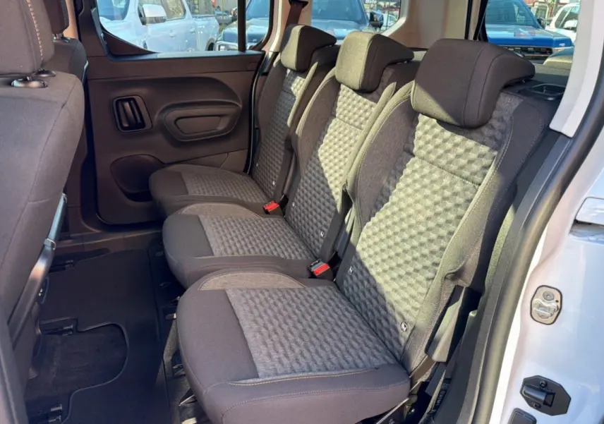 Vue latérale des sièges arrière en tissu gris du Peugeot Rifter Blanc Kaolin 2025, porte arrière ouverte.