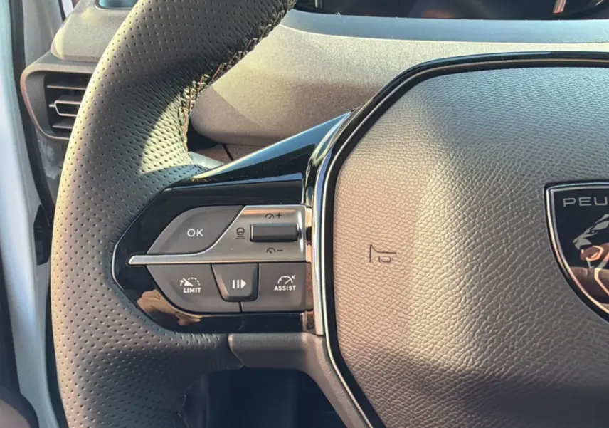 Gros plan sur le volant cuir perforé du Peugeot Rifter blanc kaolin, avec commandes multifonctions et logo lion central.