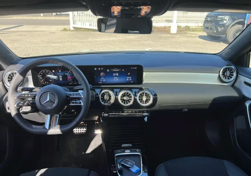 Vue intérieure frontale du tableau de bord de la Mercedes Classe A 200D Exclusive Design avec écran large et volant cuir multifonctions.