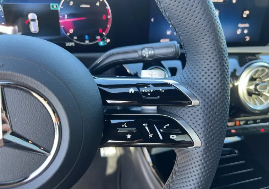 Gros plan sur le volant cuir perforé à commandes multifonctions d’une Mercedes Classe A 200D 2026, tableau de bord digital en arrière-plan.