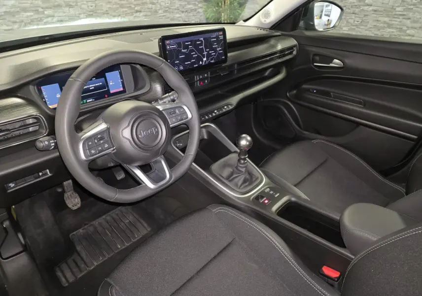 Vue intérieure côté conducteur du Jeep Avenger 2025, tableau de bord noir avec écran tactile et levier de vitesses manuel.