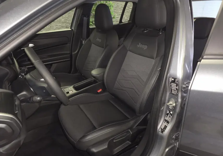 Vue intérieure côté conducteur du Jeep Avenger gris 2025, sièges noirs avec logo Jeep brodé sur appuie-tête.