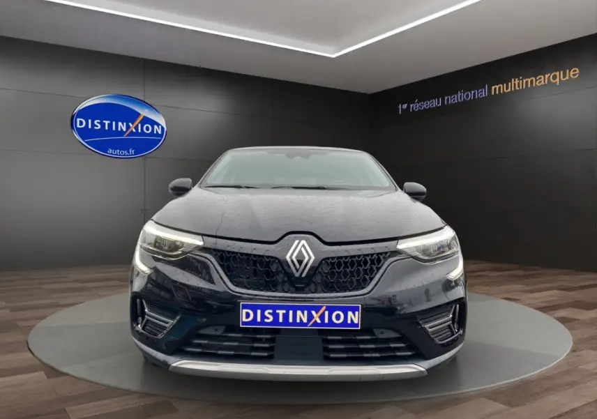 Vue frontale d'une Renault Arkana noire 2024 avec calandre hexagonale et feux LED distinctifs, sur podium intérieur.