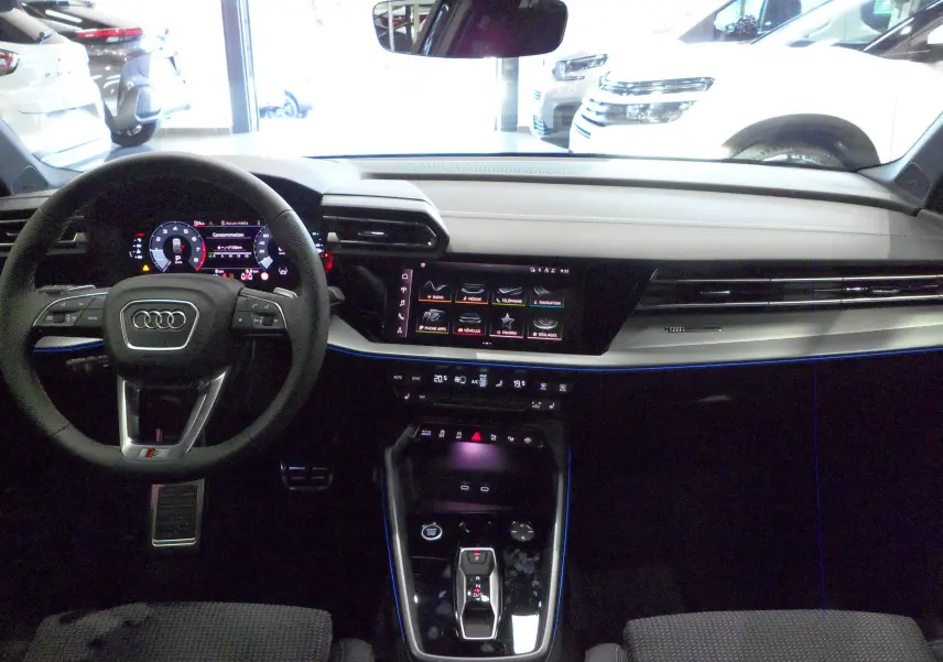 Vue intérieure de l'Audi A3 Sportback 2025, tableau de bord moderne avec écran tactile et volant multifonction noir.