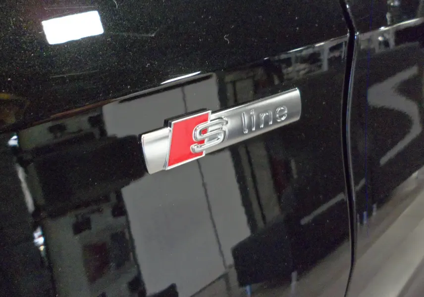 Gros plan sur l'emblème S line argent et rouge sur la porte noire Mythe d'une Audi A3 Sportback 2025
