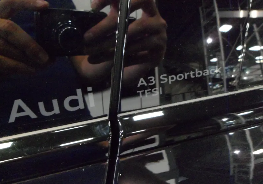 Gros plan sur l'inscription A3 Sportback TFSI sur la porte noire Mythe d'une Audi 2025, reflet d'un photographe visible.