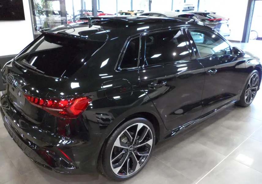 Audi A3 Sportback noir Mythe vue 3/4 arrière droit en intérieur avec jantes alliage bicolores et vitres teintées.