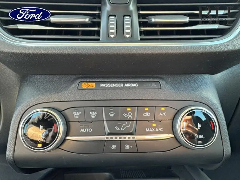 Tableau de bord du Ford Kuga gris Solar 2023, zoom sur commandes climatisation automatique bi-zone et indicateur airbag passager.