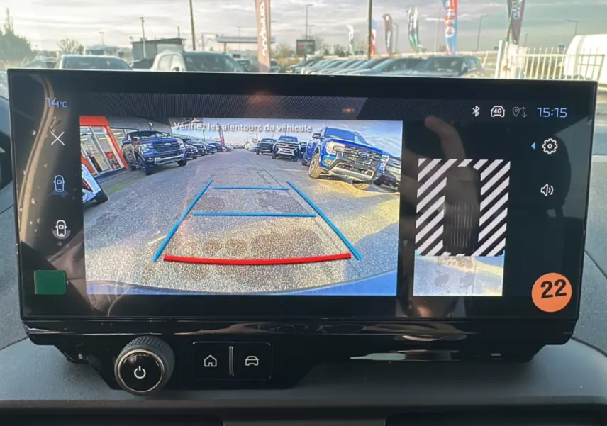 Écran tactile intérieur montrant la caméra de recul avec vue arrière sur un parking ensoleillé.