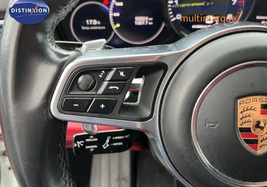 Gros plan sur le volant noir multifonction avec logo Porsche, montrant les commandes et palettes de la Panamera 4 E-Hybrid blanche.